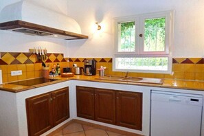 A compact kitchen with a built-in dishwasher, a window with a view of greenery, and a wall-mounted knife rack. - with pool in the hinterland of the coast (Flayosc)
