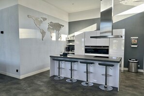 A modern kitchen with a central island, bar stools, a stainless steel range hood, and a world map on the wall. - Holiday home with 3 bedrooms (Heerhugowaard)