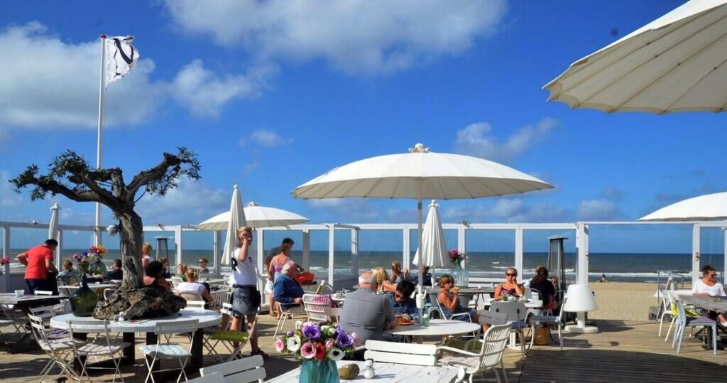 An outdoor dining area with tables and umbrellas, overlooking the sea.