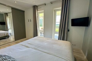 Ein Schlafzimmer mit einem großen Bett, einem an der Wand montierten Fernseher und einer Schiebetür, die auf einen Balkon führt.