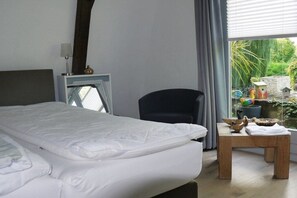 Ett hotellrum med en säng, en stol, ett litet bord med dekorativa föremål och utsikt över grönområden utanför.