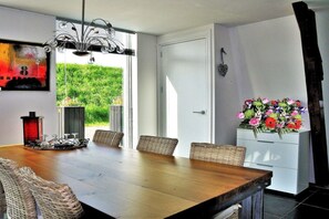 En matplats med ett träbord, flätade stolar, en kristallkrona och utsikt över grönskan utanför.