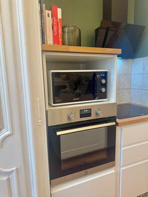 A kitchen with a built-in oven and microwave, a shelf with books, and a decorative item.