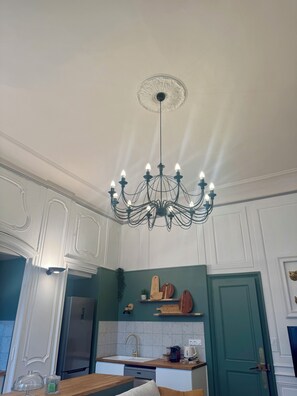 A kitchen with white cabinetry, a green accent wall, a chandelier, and a stainless steel refrigerator.