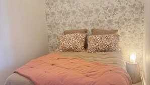 Ein Schlafzimmer mit einem Bett, blumigem Wandpapier, einer Nachttischlampe und einer Pendelleuchte.