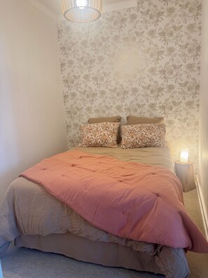 Quarto com cama, papel de parede floral, luminária de cabeceira e lustre.