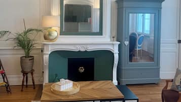 Un salon avec une cheminée, un lustre, un buffet bleu et une table basse en bois.