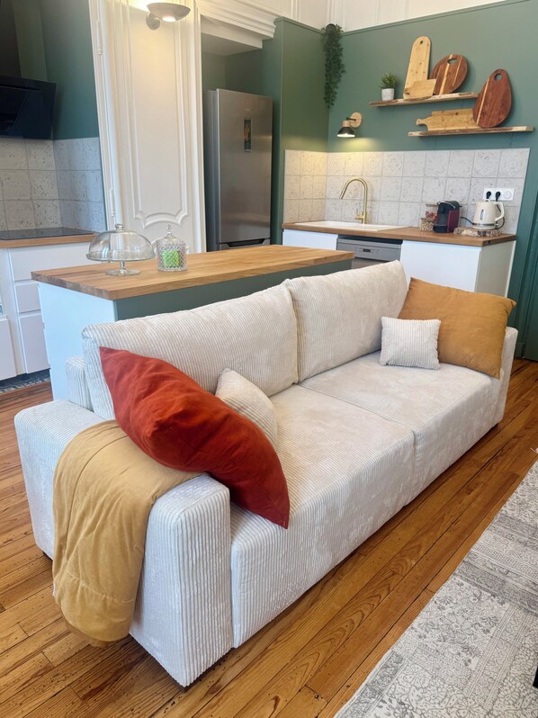 A modern kitchen with a central island, a sofa with cushions, and a wooden floor.