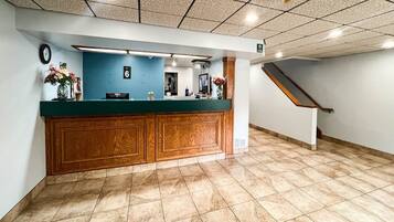 A reception area with a wooden counter, a clock, and a staircase leading to an upper level.