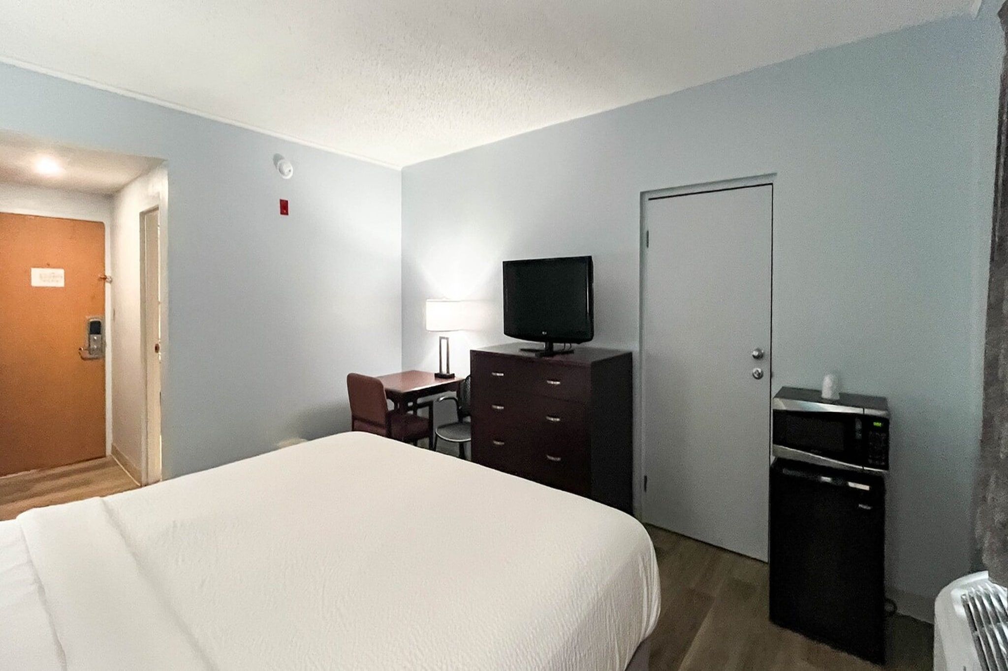 Une chambre d’hôtel comprenant un lit, un bureau avec une chaise, une télévision, une commode et une porte.
