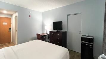Une chambre d’hôtel comprenant un lit, un bureau avec une chaise, une télévision, une commode et une porte.