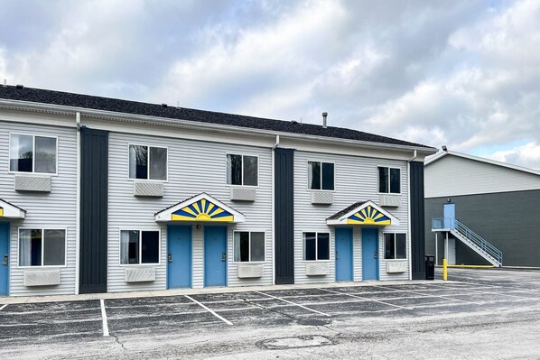 A motel with a row of rooms, each with a blue door and a sun emblem above the door.