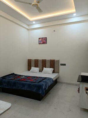 A bedroom with a bed, a ceiling fan, recessed lighting, and a small painting on the wall. - Om Mukunda Homestay (Ujjain)