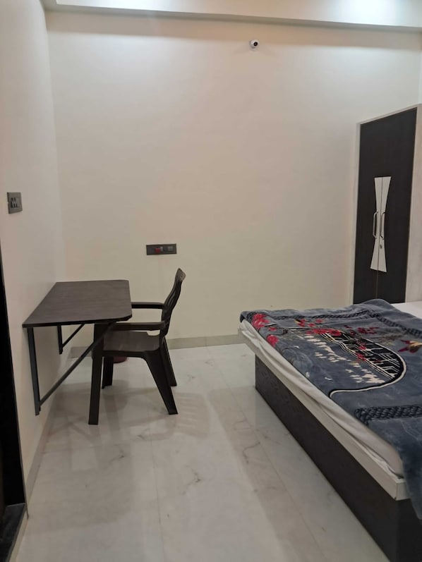 A small room with a bed, a desk, and a chair. - Om Mukunda Homestay (Ujjain)