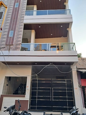 A multi-story residential building with a balcony, a garage door, and a motorcycle parked in front. - Om Mukunda Homestay (Ujjain)