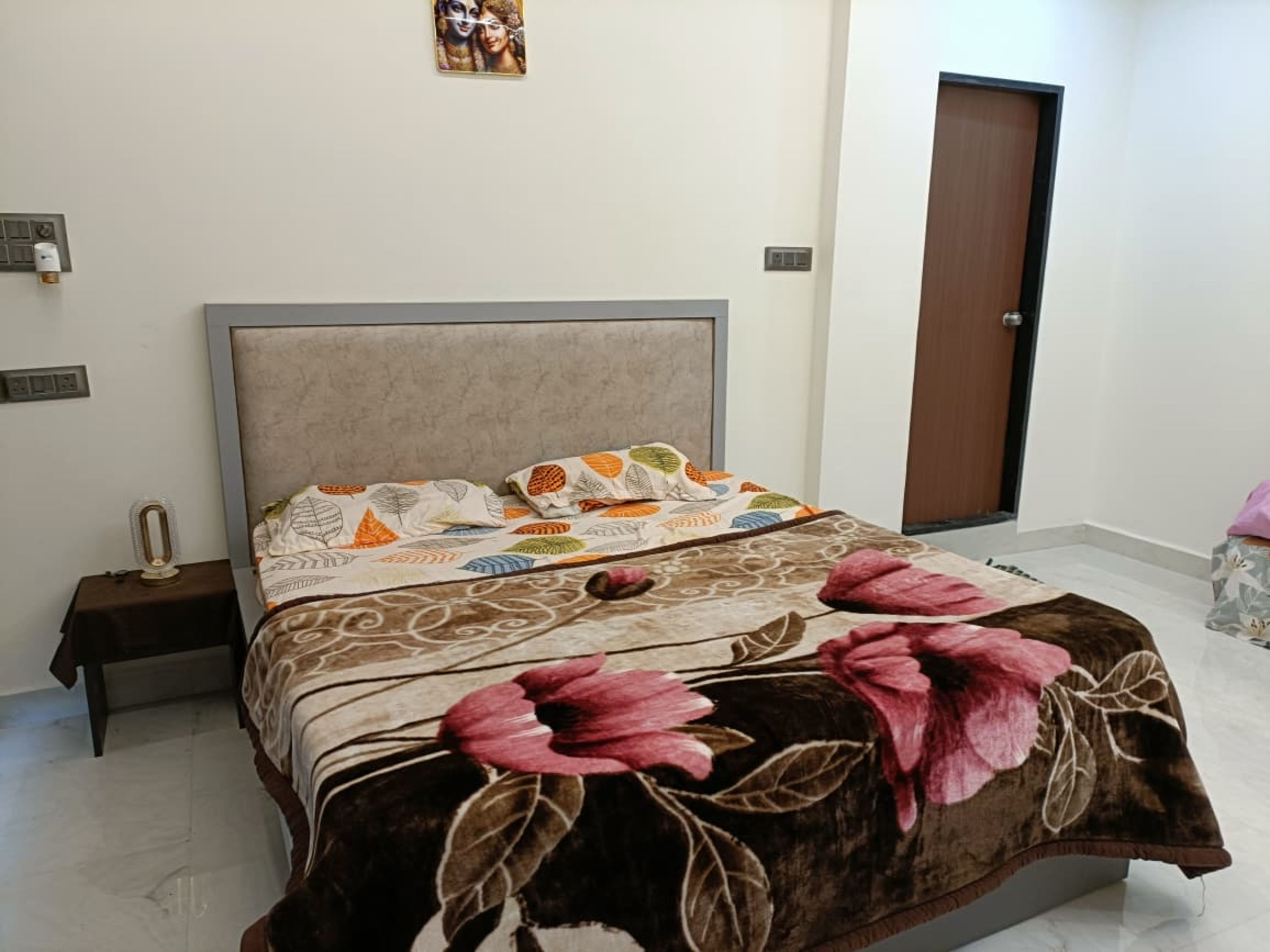 Quarto com cama, mesa de cabeceira, tomada e porta.