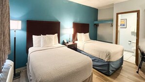 Et hotelværelse med to senge, et natbord, en lampe og et badeværelse, der kan ses gennem en åben dør.