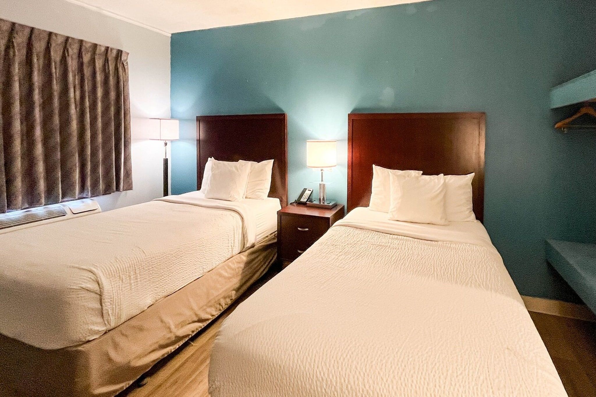 A hotel room with two beds, a nightstand, a lamp, and a window with curtains.