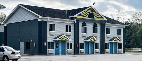 En tvåvåningsbyggnad med ett garage på vänster sida, ett takförsett parkeringsområde och en rad dörrar med en karakteristisk solstråledesign.