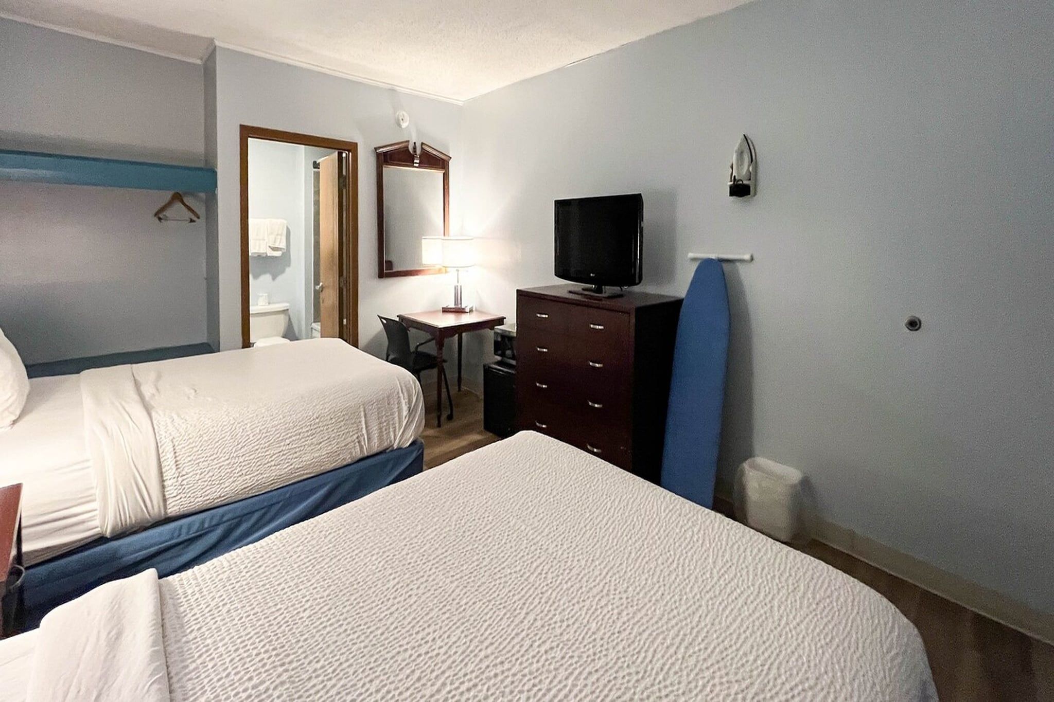 Habitación de hotel con dos camas, un escritorio, una silla, un aparador, un televisor y un espejo.