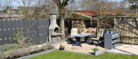 Een achtertuin met een barbecueplaats, een stenen open haard en een houten omheining.