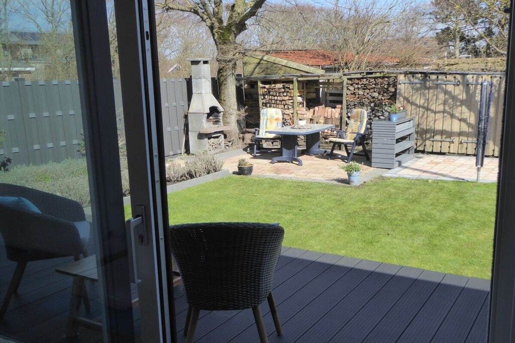 Une terrasse avec une chaise en osier, une table et un barbecue à l’arrière-plan.