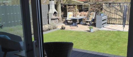 Une terrasse avec une chaise en osier, une table et un barbecue à l’arrière-plan.