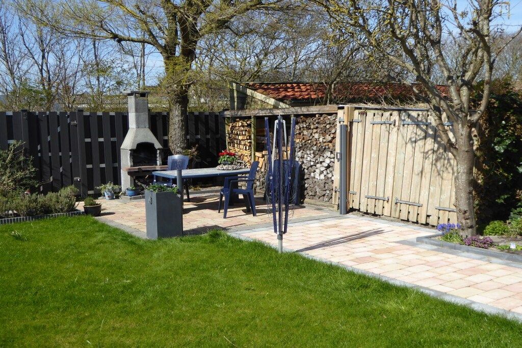 Een achtertuin met een barbecue, een eettafel en een overdekte zithoek.