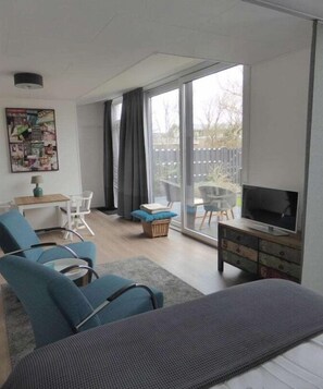 Ein modernes Wohnzimmer mit einer Couch, einem Fernseher und einer Glastür, die auf einen Balkon führt.