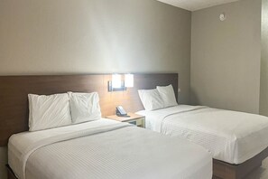 Une chambre d’hôtel avec deux lits, une table de chevet avec un téléphone et des lampes fixées au mur.