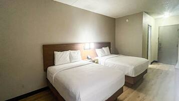 Une chambre d’hôtel avec deux lits, une table de chevet avec un téléphone et une porte donnant sur une autre chambre.