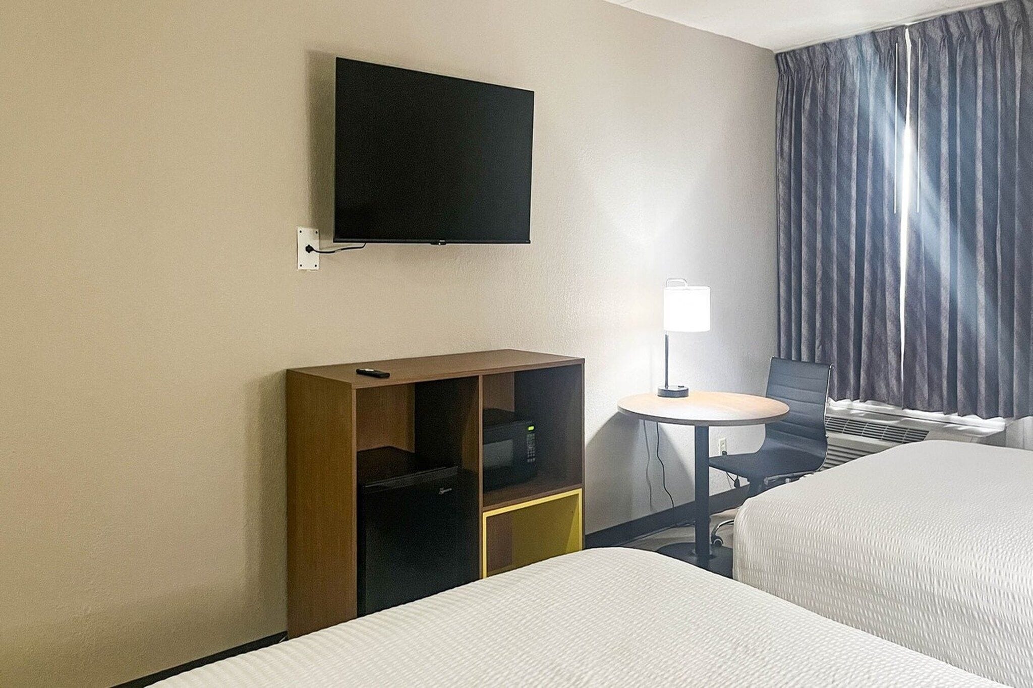 Una habitación de hotel con televisión en la pared, un escritorio con lámpara y una cama.