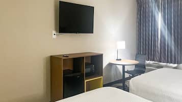Una habitación de hotel con televisión en la pared, un escritorio con lámpara y una cama.