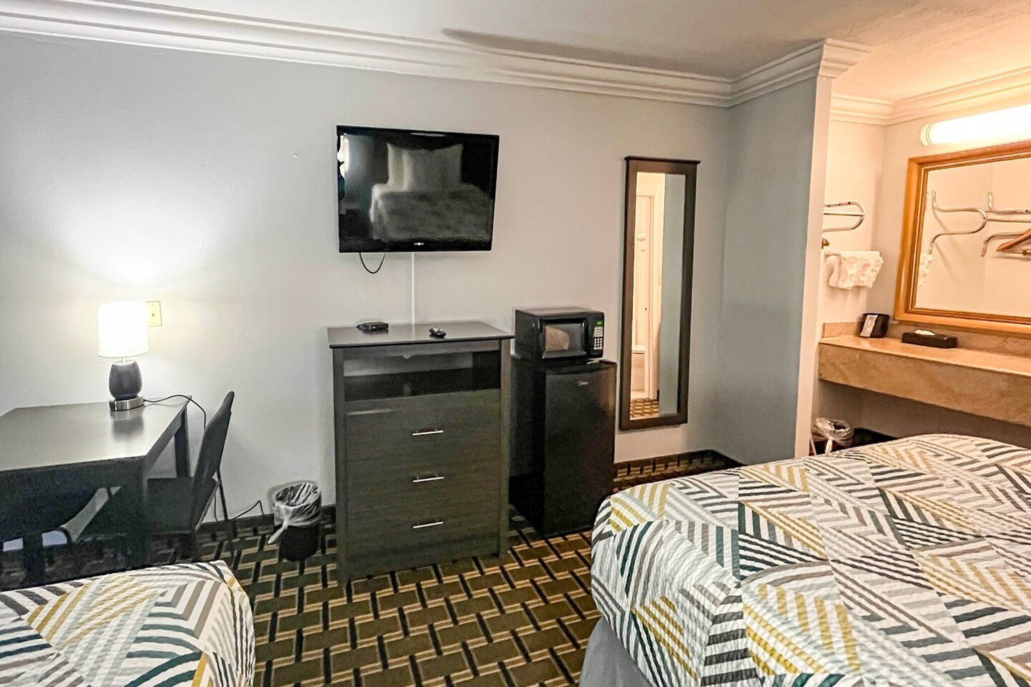 Una habitación de hotel con una cama, un escritorio, un televisor, un espejo y un microondas.
