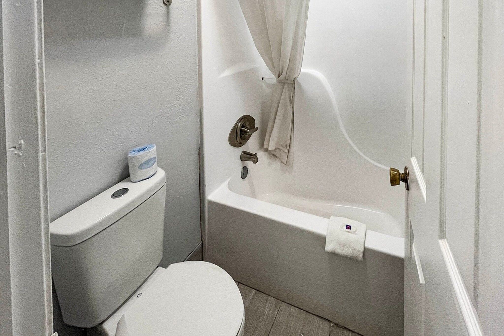 Een kleine, praktische badkamer met toilet, bad en douchegordijn.