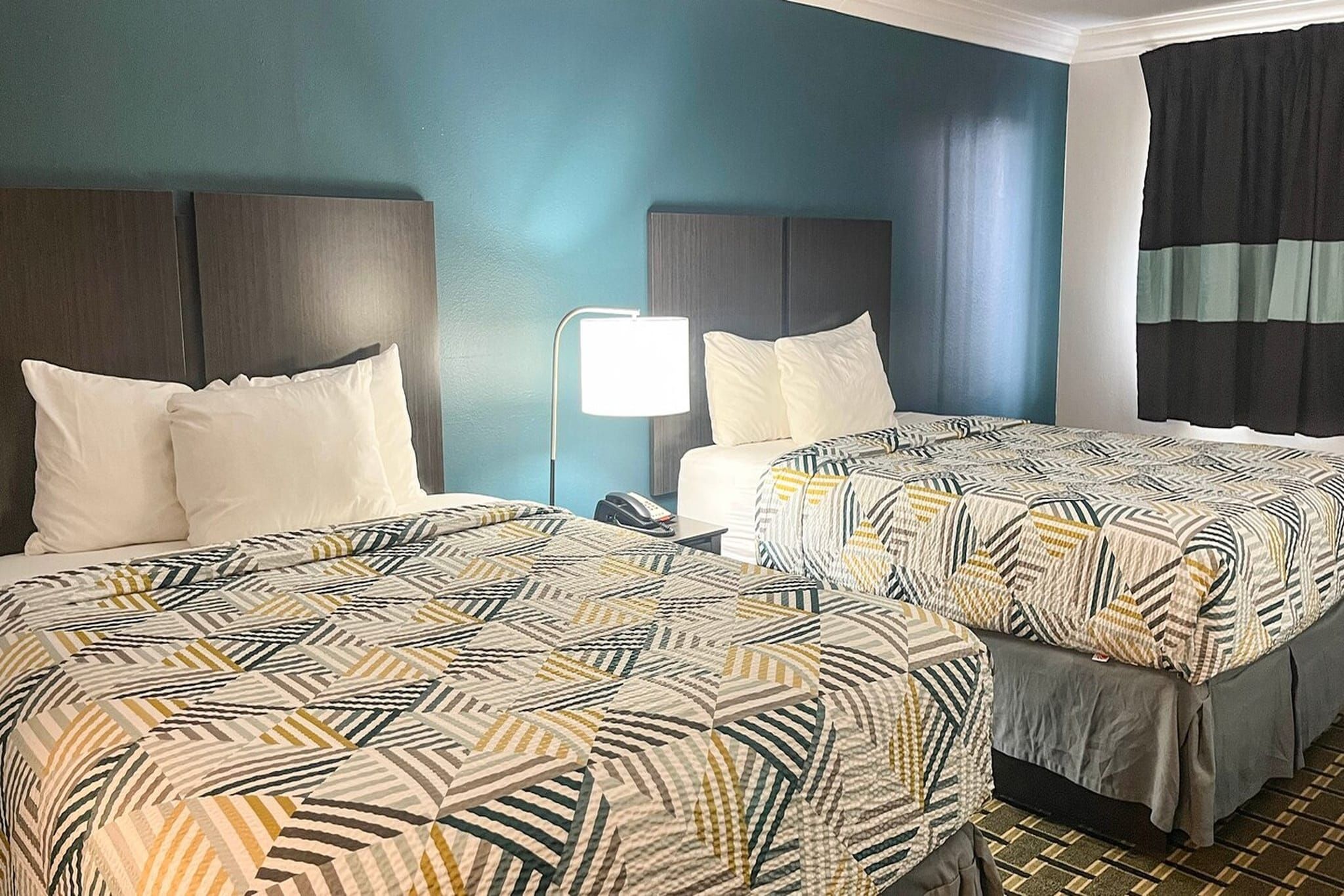 Een hotelkamer met twee bedden, een nachtkastje met een lamp en een raam met gordijnen.