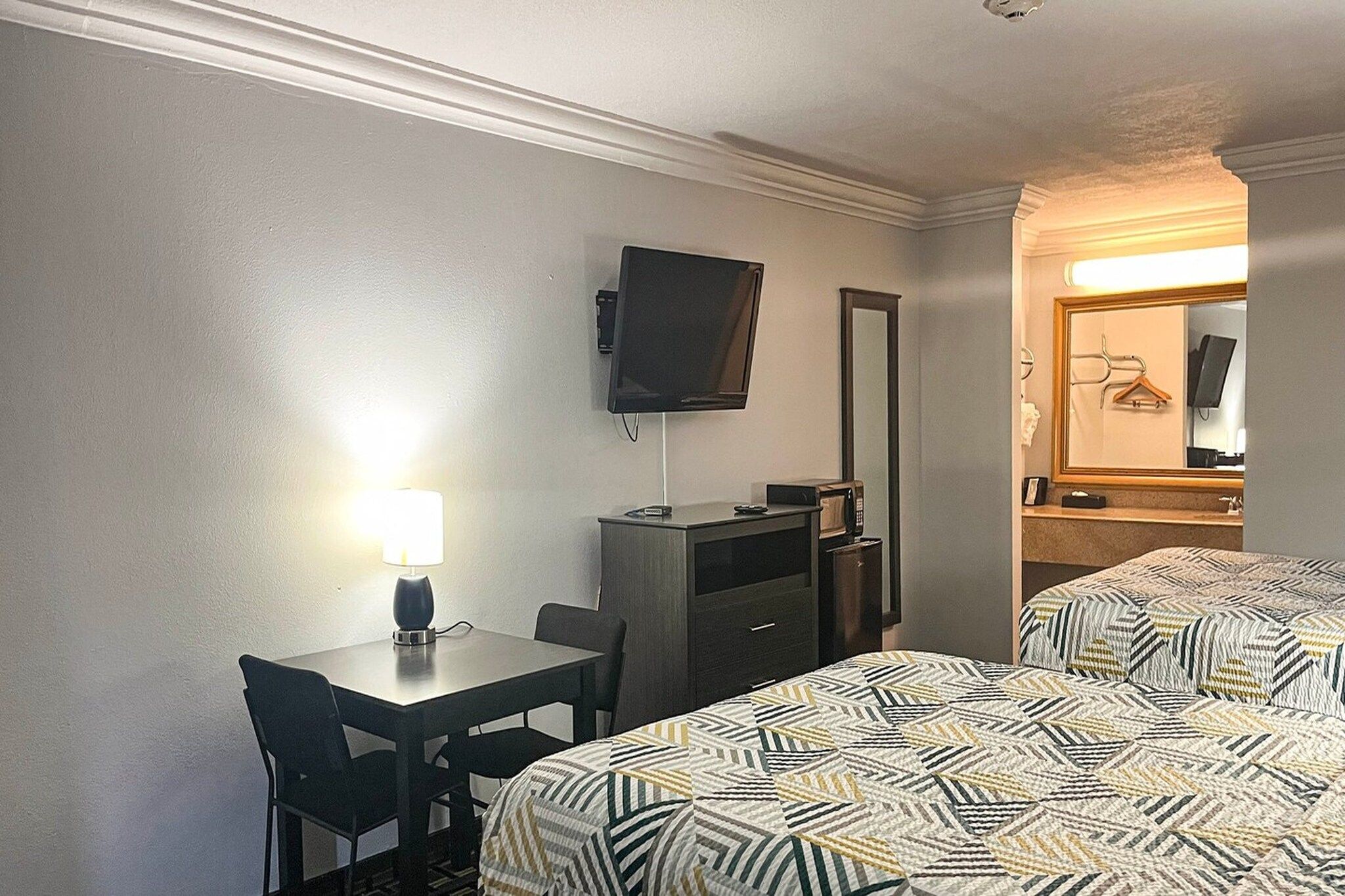 Een hotelkamer met een bed, een bureau, een stoel, een televisie, een spiegel en een lamp.