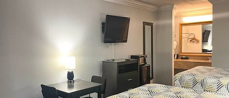 A hotel room with a bed, a desk, a chair, a television, a mirror, and a lamp.