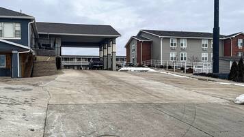 A parking area with a covered section, adjacent buildings, and a tall structure.