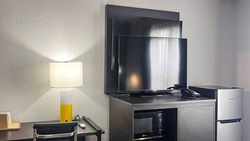 A hotel room with a flat-screen TV mounted on the wall, a desk with a lamp, and a minibar.