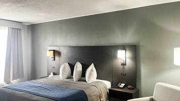 A hotel room with a bed, bedside tables, a chair, and a wall-mounted lamp.