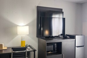 Habitación de hotel con televisor de pantalla plana en la pared, un escritorio con lámpara y un minibar.