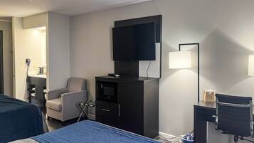 A hotel room with a bed, a desk, a chair, a television, and a wall-mounted lamp.