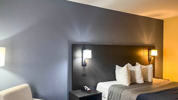 Et hotelværelse med seng, natbord, lampe og en stol.