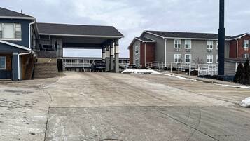 A parking area with a covered section, adjacent buildings, and a tall structure.