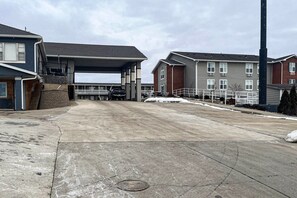 A parking area with a covered section, adjacent buildings, and a tall structure.