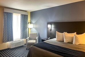 A hotel room with a bed, a chair, a bedside table with a lamp, and a wall-mounted phone.