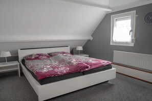 Ein Schlafzimmer mit einem weißen Bett, grauen Wänden, einem Fenster und einer weißen Heizung.