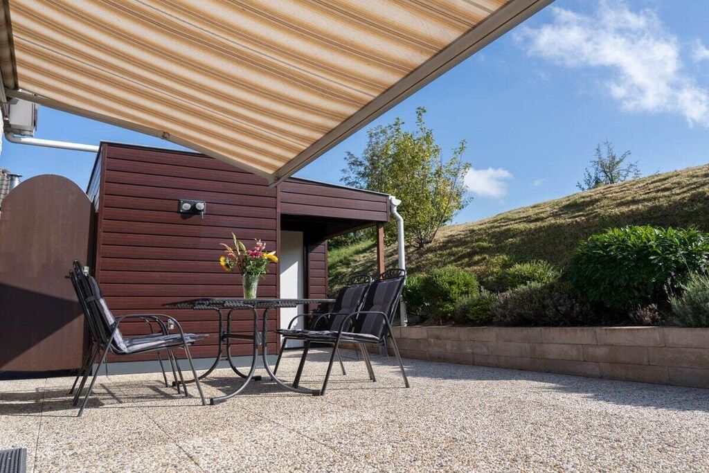 Un área de estar al aire libre con mesa y sillas, una pérgola de madera y vistas a un paisaje montañoso.