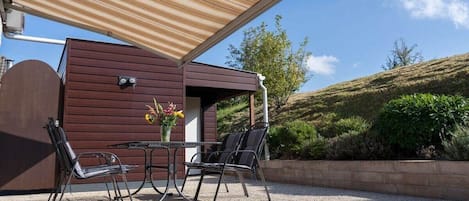 An outdoor seating area with a table and chairs, a wooden pergola, and a view of a hilly landscape.